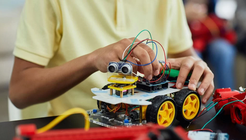 young boy in a yellow shirt plugging wires into a battery powered device