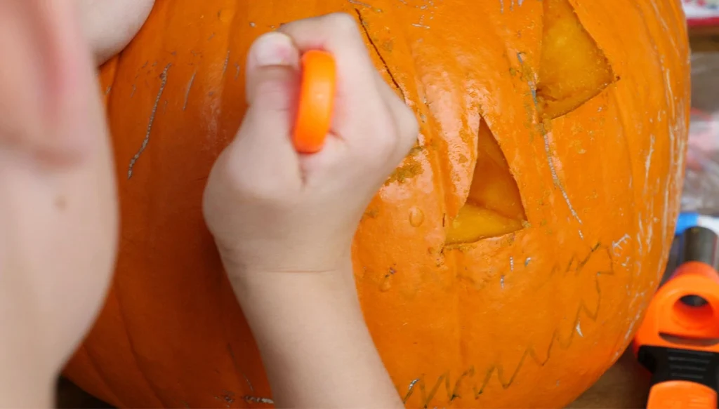 hand with a knife carving a pumpkin