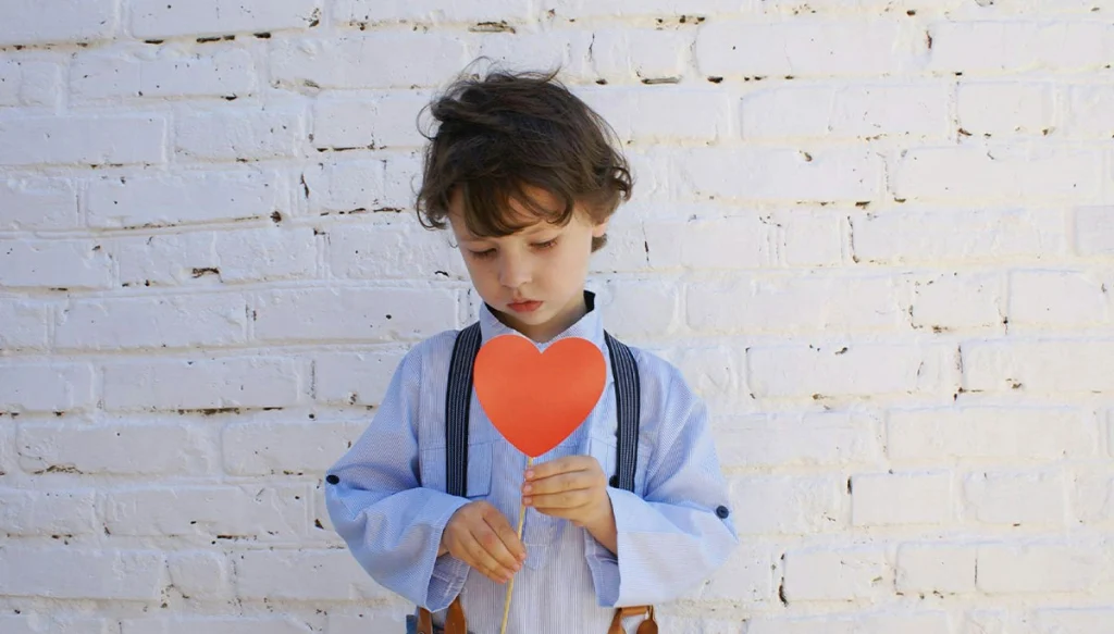young boy looks down holding a paper heart
